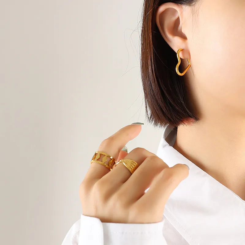 Gold heart huggie earrings and geometric rings on a woman's hand.