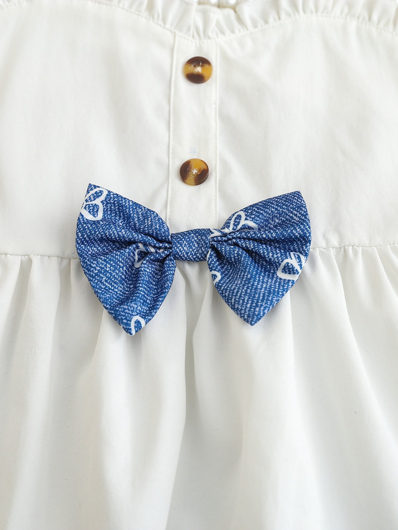 White cotton cami with sweetheart neckline, button front, and blue patterned bow detail.
