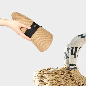 Rolled beige woven straw sun hat with black band, held by hand.