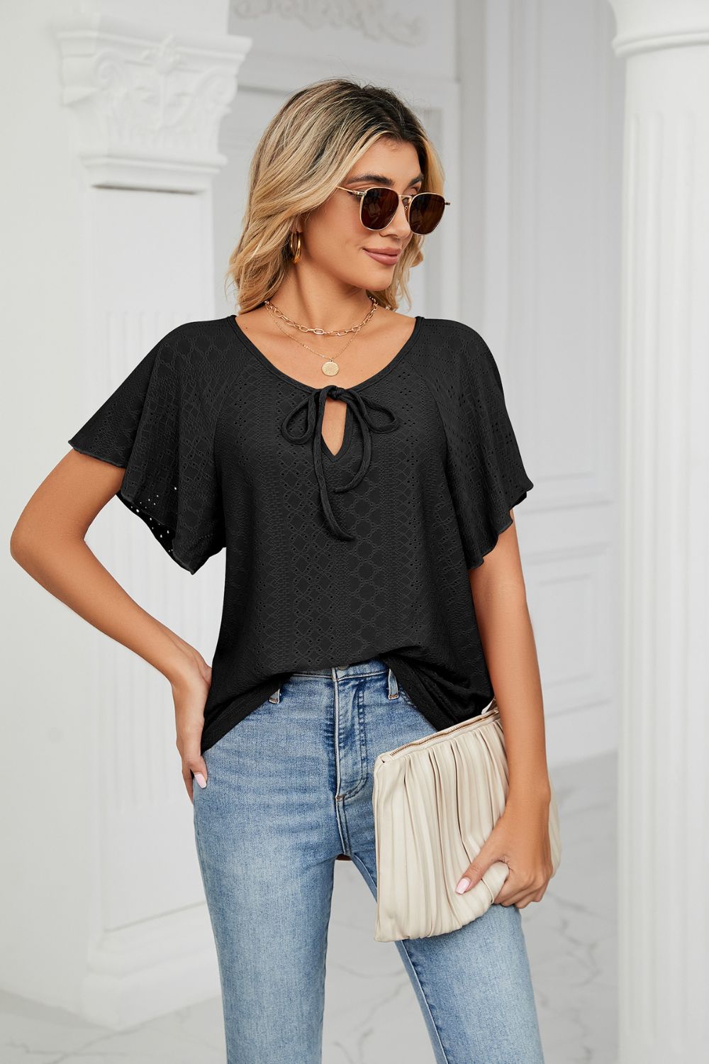 Black eyelet tie-neck blouse with flutter sleeves and a textured pattern.