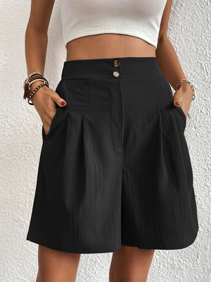 Black pleated front bermuda shorts with a textured fabric and button closure.
