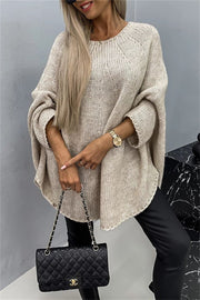 Relaxed knit sweater in Khaki with cape sleeves and a crew neck, styled with black pants and a quilted handbag.
