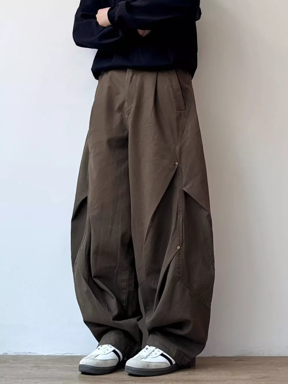 Men's brown loose fit cargo pants with pleated details and button closures.