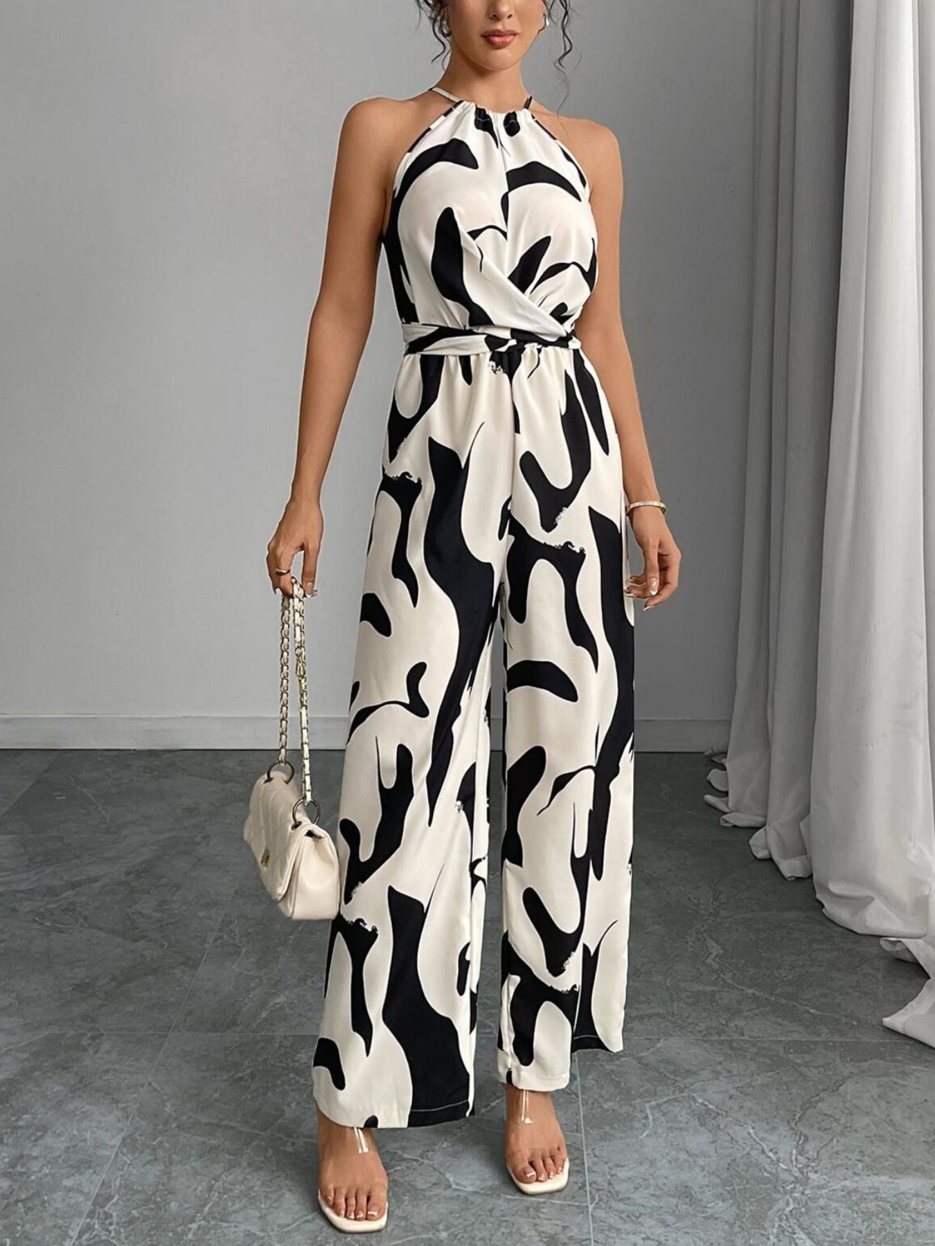 Chic abstract print halter jumpsuit in black and white with a tie waist and wide legs.