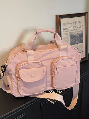 Pink nylon duffle bag with adjustable strap and multiple front pockets.