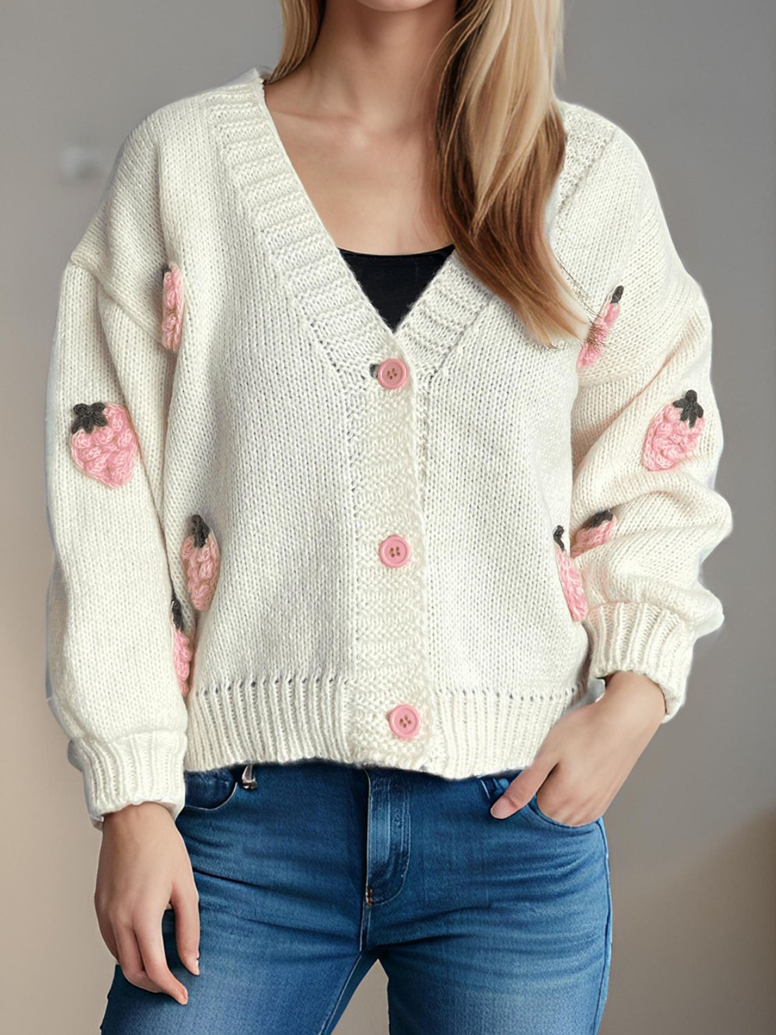 White knit cardigan with pink strawberry appliqués and buttons, V-neck, long sleeves.