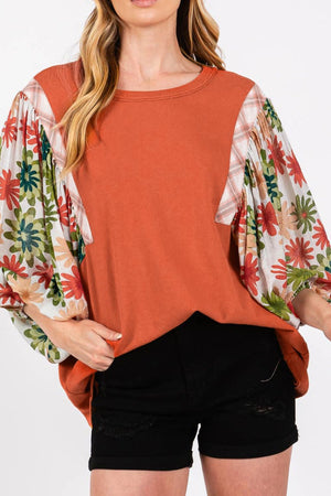 Orange-red blouse with floral patchwork balloon sleeves and plaid accents.