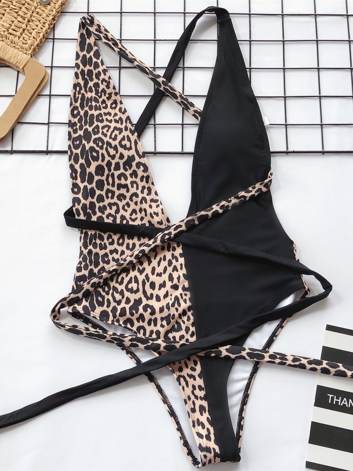 One-piece swimsuit with leopard print and black panels, featuring a wrap detail and crisscross straps.