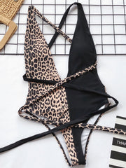 One-piece swimsuit with leopard print and black panels, featuring a wrap detail and crisscross straps.