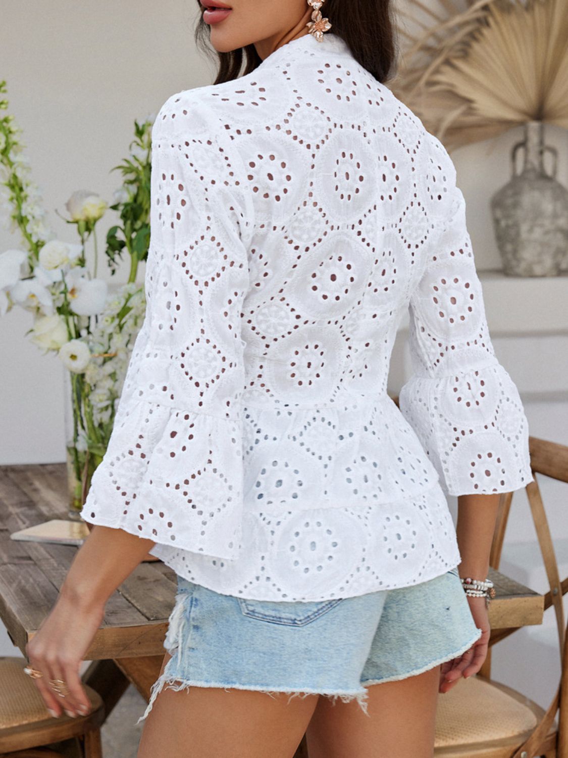 White eyelet embroidered peplum blouse with ruffled bell sleeves and buttoned front.