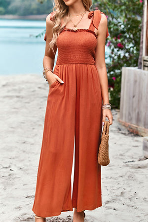 Orange smocked bodice tie-strap palazzo jumpsuit with wide legs and pockets.