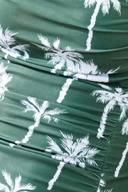 Dark green one-piece swimsuit with white palm tree print and ruching detail.