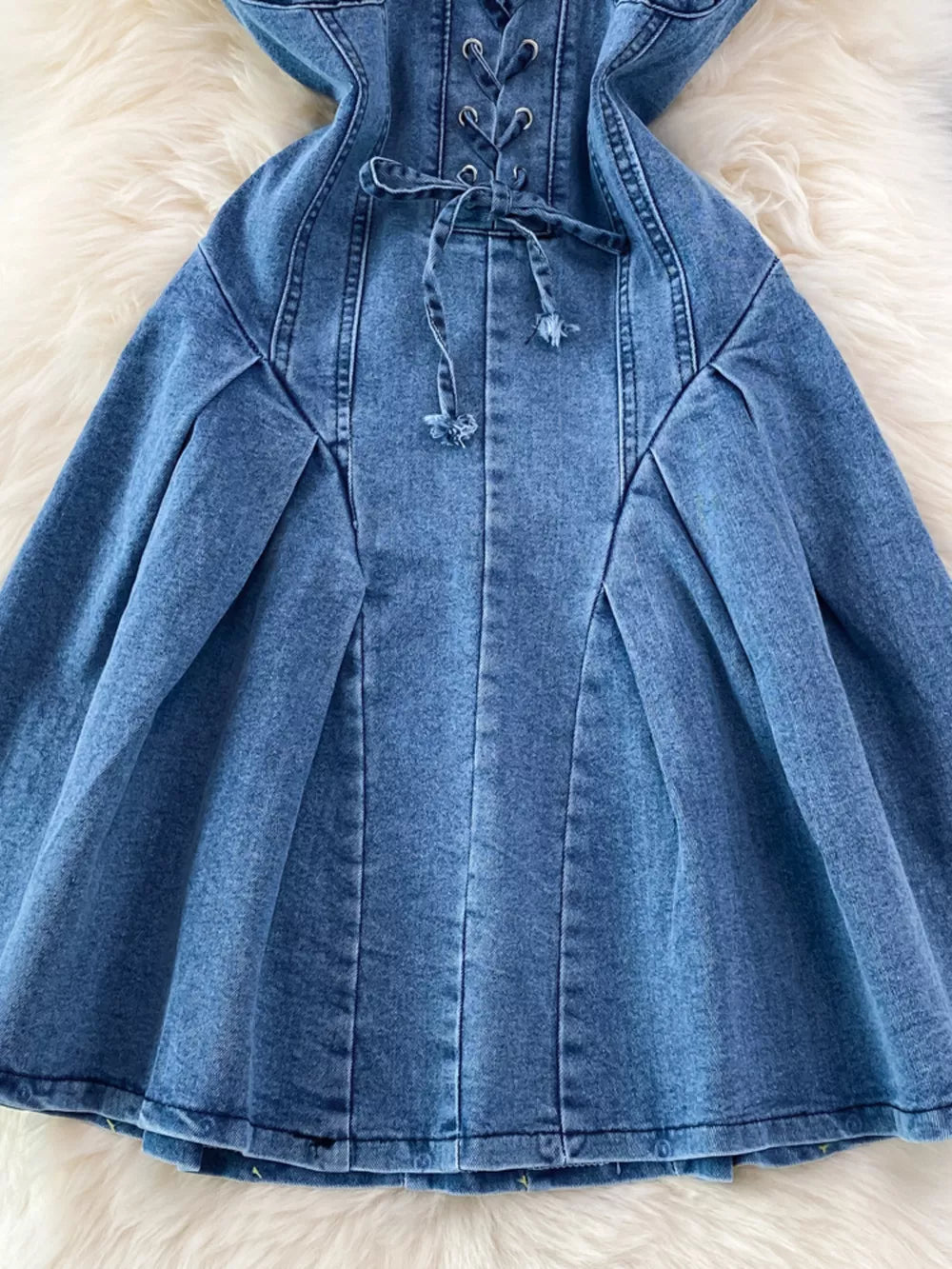 Blue denim A-line dress with lace-up corset detail and pleated skirt.