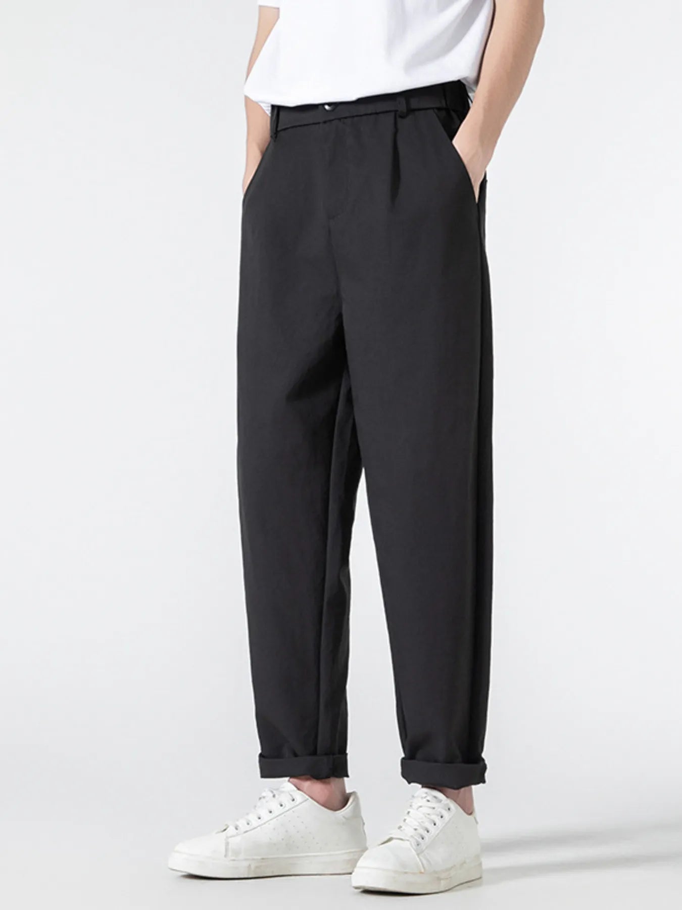 Black casual pleated trousers with a loose fit and cuffed hems, styled with white sneakers.