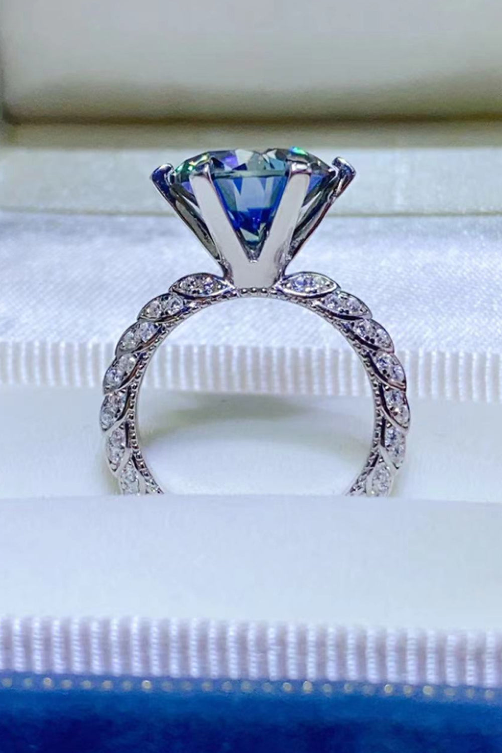 Blue solitaire engagement ring with pavé band and large faceted blue gemstone.