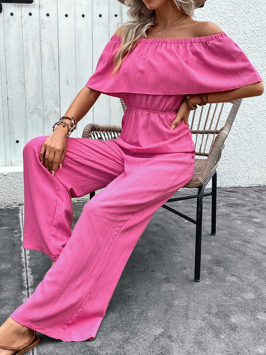 Hot pink off-the-shoulder ruffled waist jumpsuit with wide legs.