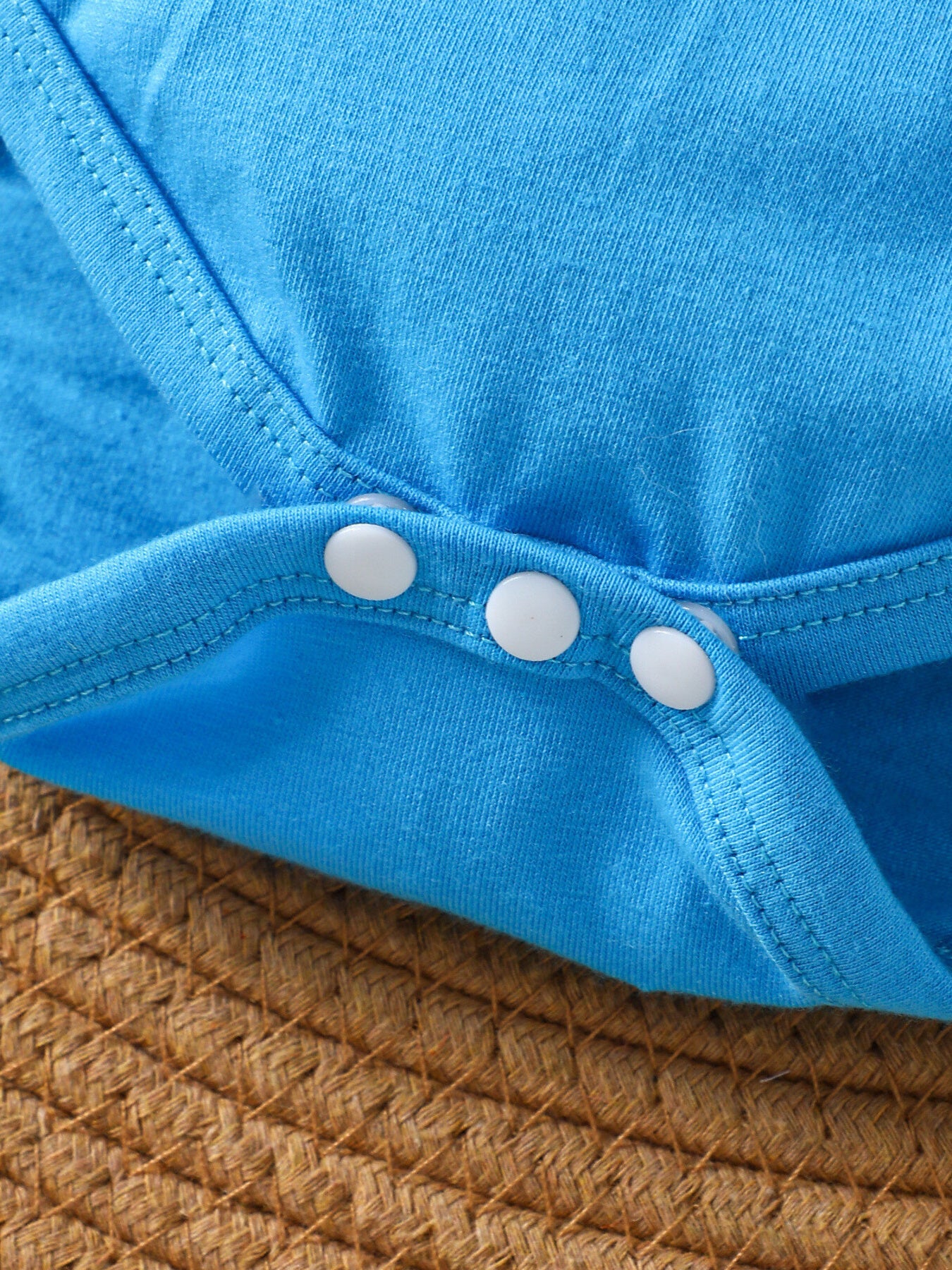 Blue cotton baby bodysuit with white snaps, close-up detail
