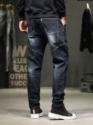 Men's dark wash distressed denim jeans with slim fit and unique paneling.
