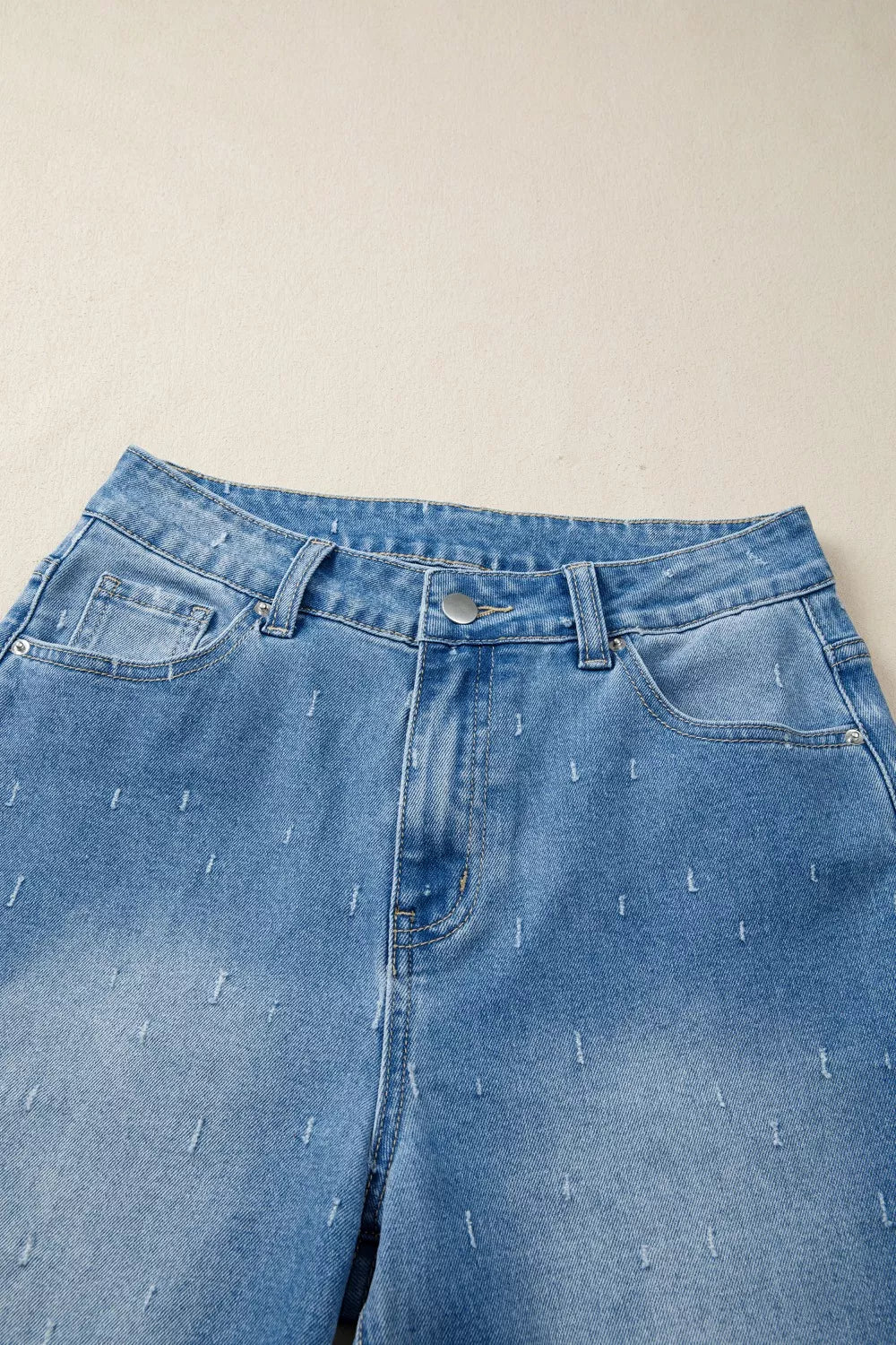 High-rise light wash denim jeans with distressed details and a raw hem.