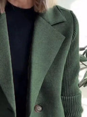 Double-breasted green trench coat with knit sleeves and a single button closure.