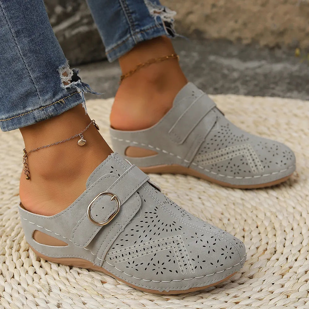 Gray laser-cut buckle mule wedges with perforated details and adjustable strap.