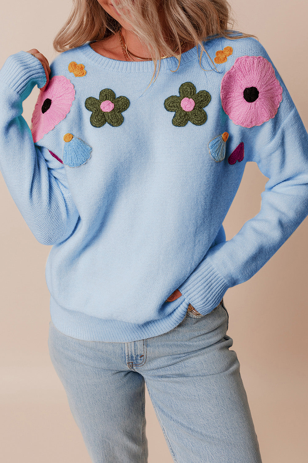 Light blue knit sweater with embroidered floral appliqués and ribbed cuffs.