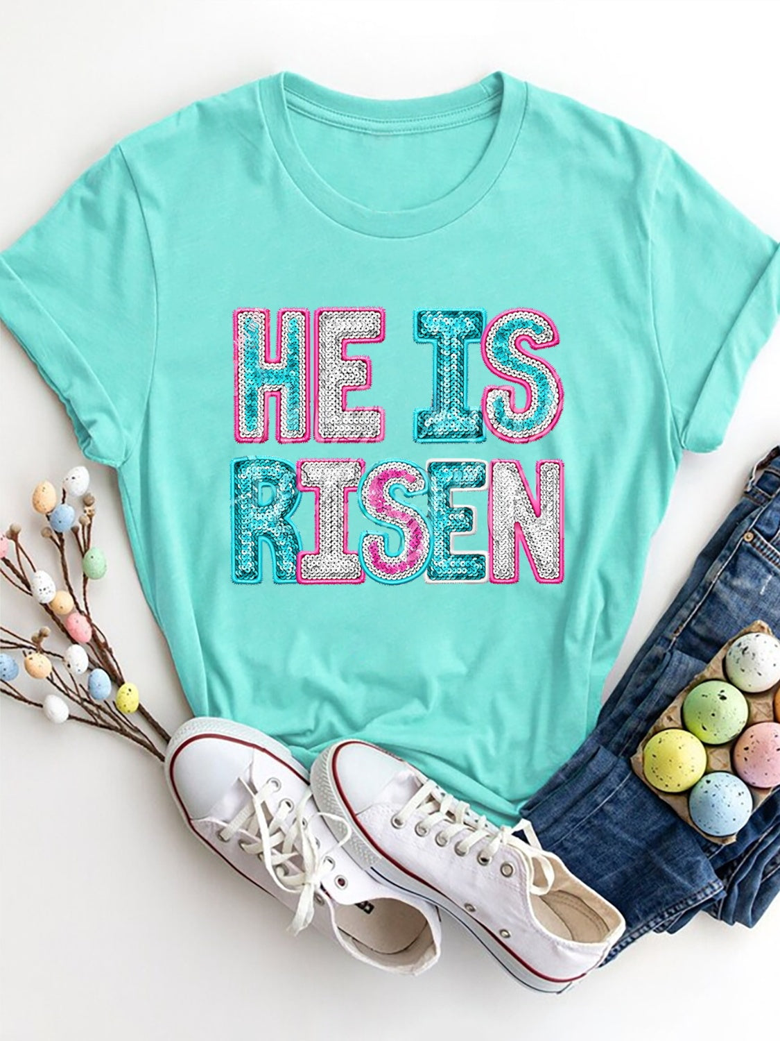 Aqua crewneck t-shirt with sequin "He Is Risen" graphic and rolled sleeves.