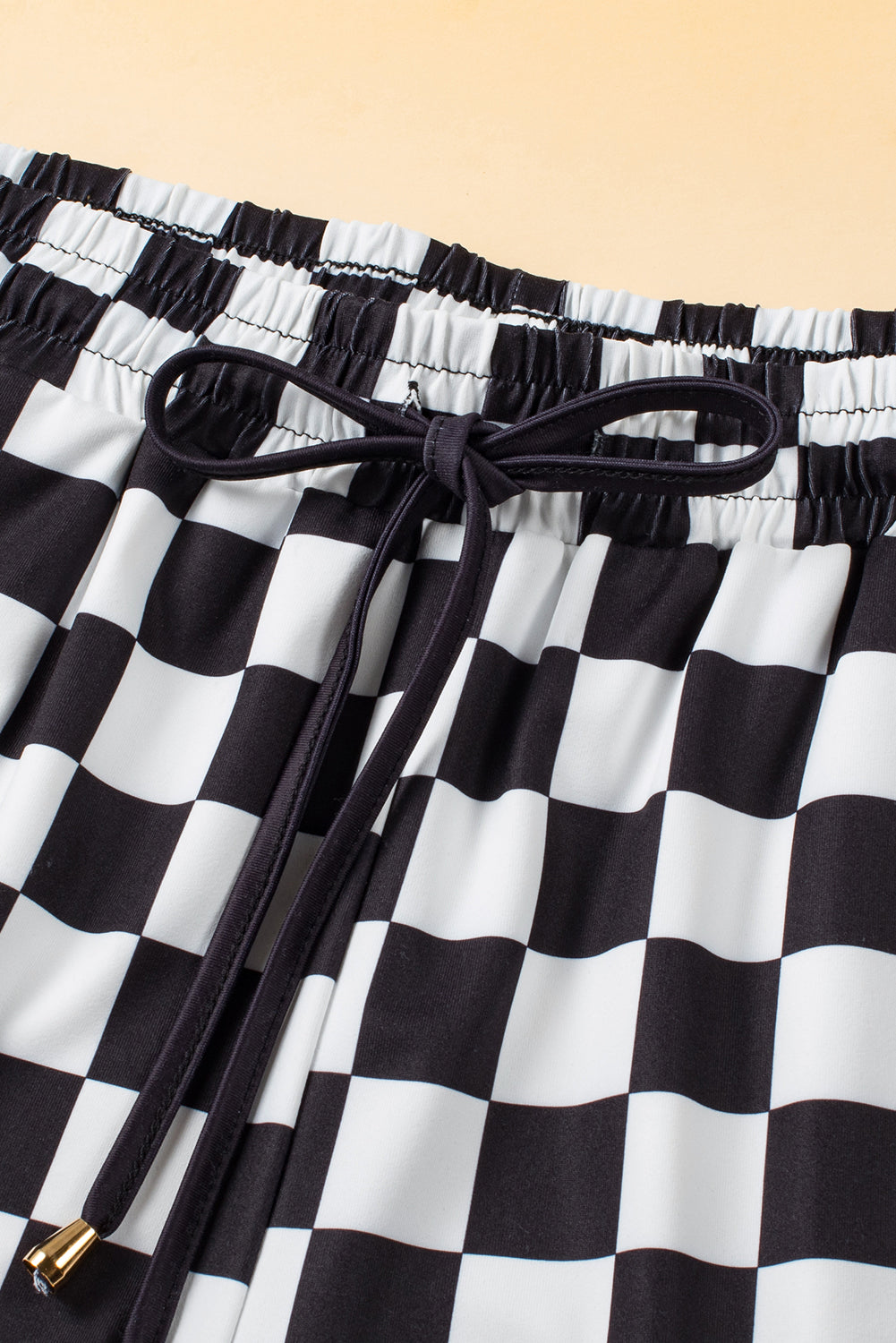 Black and white checkerboard lounge shorts with drawstring waist and gold-tipped ends.