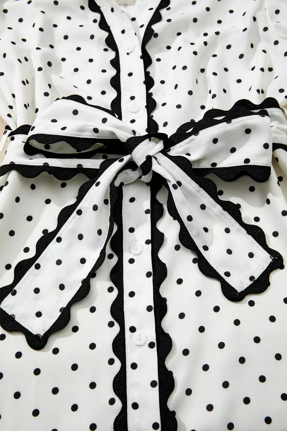 White polka dot midi dress with black scalloped trim and tie belt.