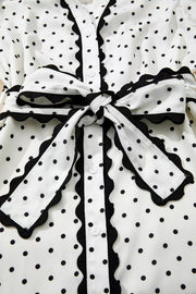 White polka dot midi dress with black scalloped trim and tie belt.