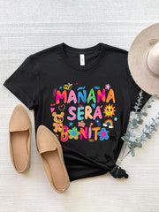 Black graphic tee with colorful "Mañana Sera Bonito" text, bee, teddy bear, sun, rainbow, and flowers.
