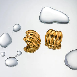 Sculptural ribbed gold earrings with 18K gold plating, displayed with water droplets.