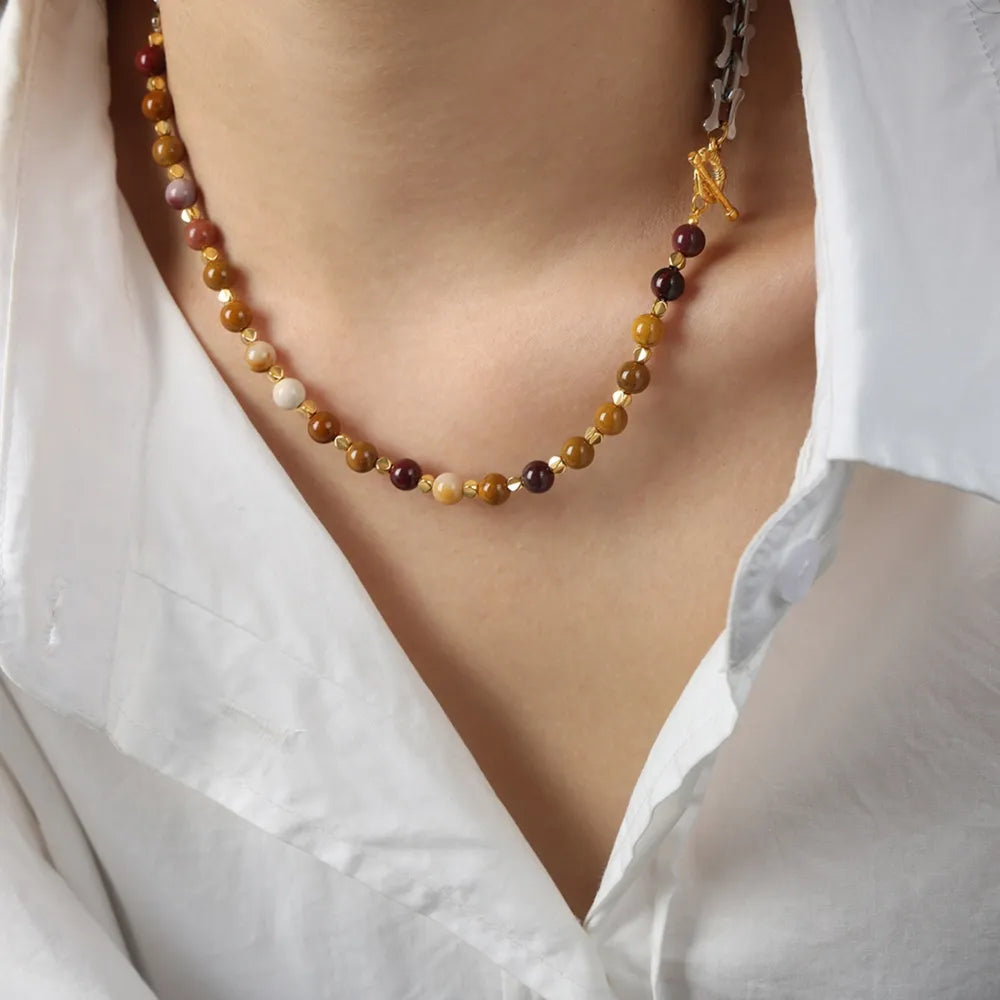 Asymmetrical bead and bone chain necklace with mixed earth-toned beads and gold accents.
