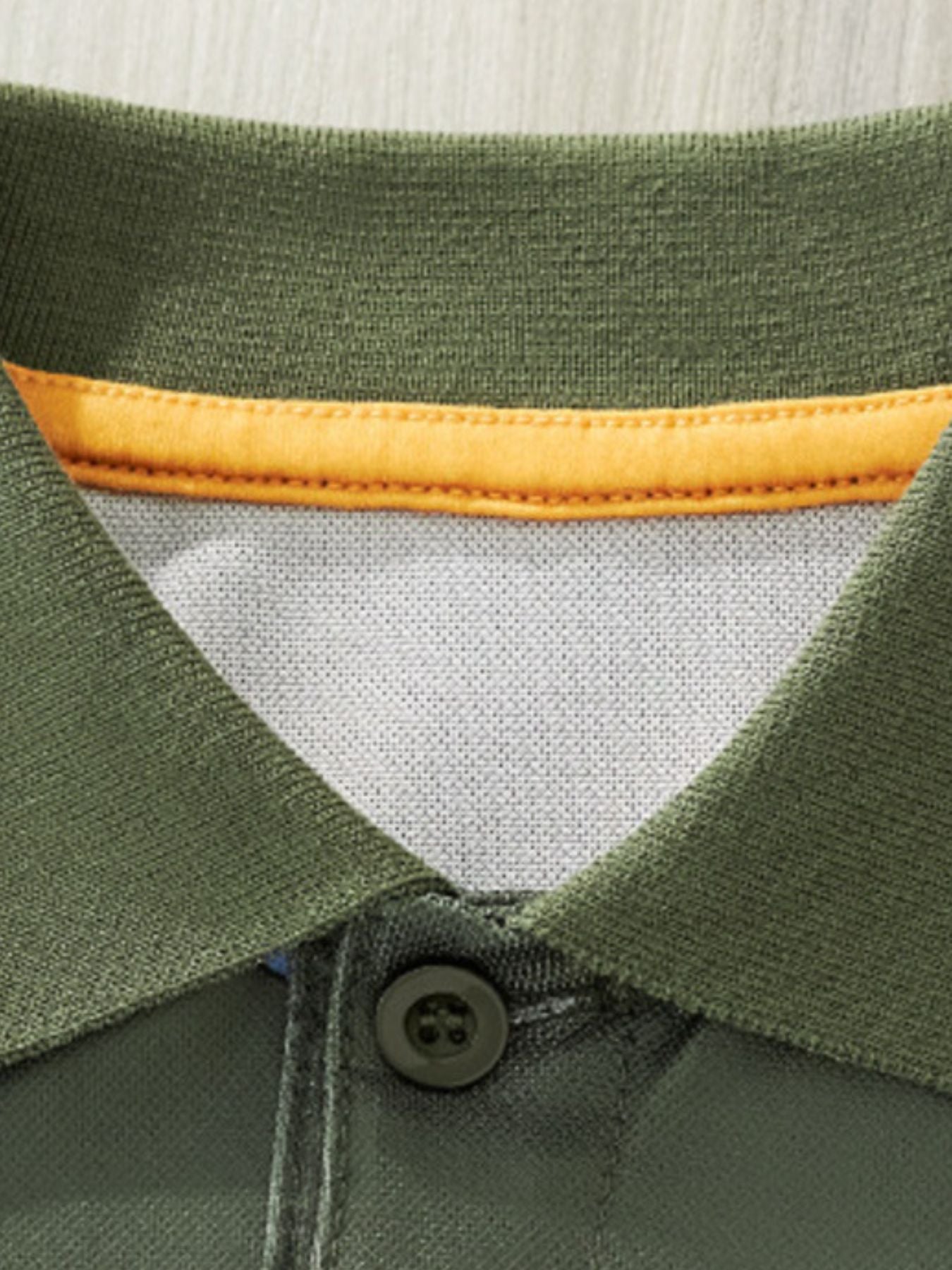 Children's green polo shirt with orange trim and a dark button.