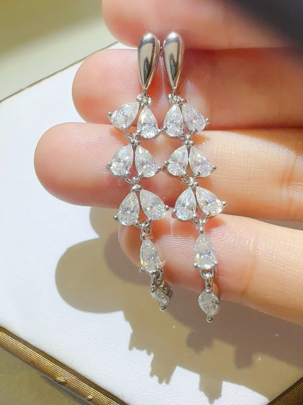 Cascading moissanite pear drop earrings in silver with multiple sparkling stones.