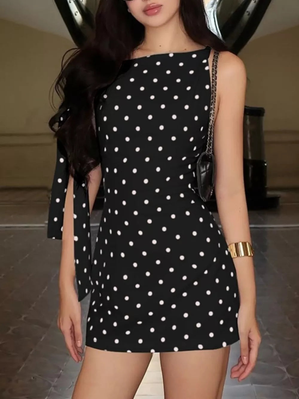 Black polka dot mini dress with asymmetrical neckline and bow sleeve details.