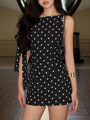 Black polka dot mini dress with asymmetrical neckline and bow sleeve details.