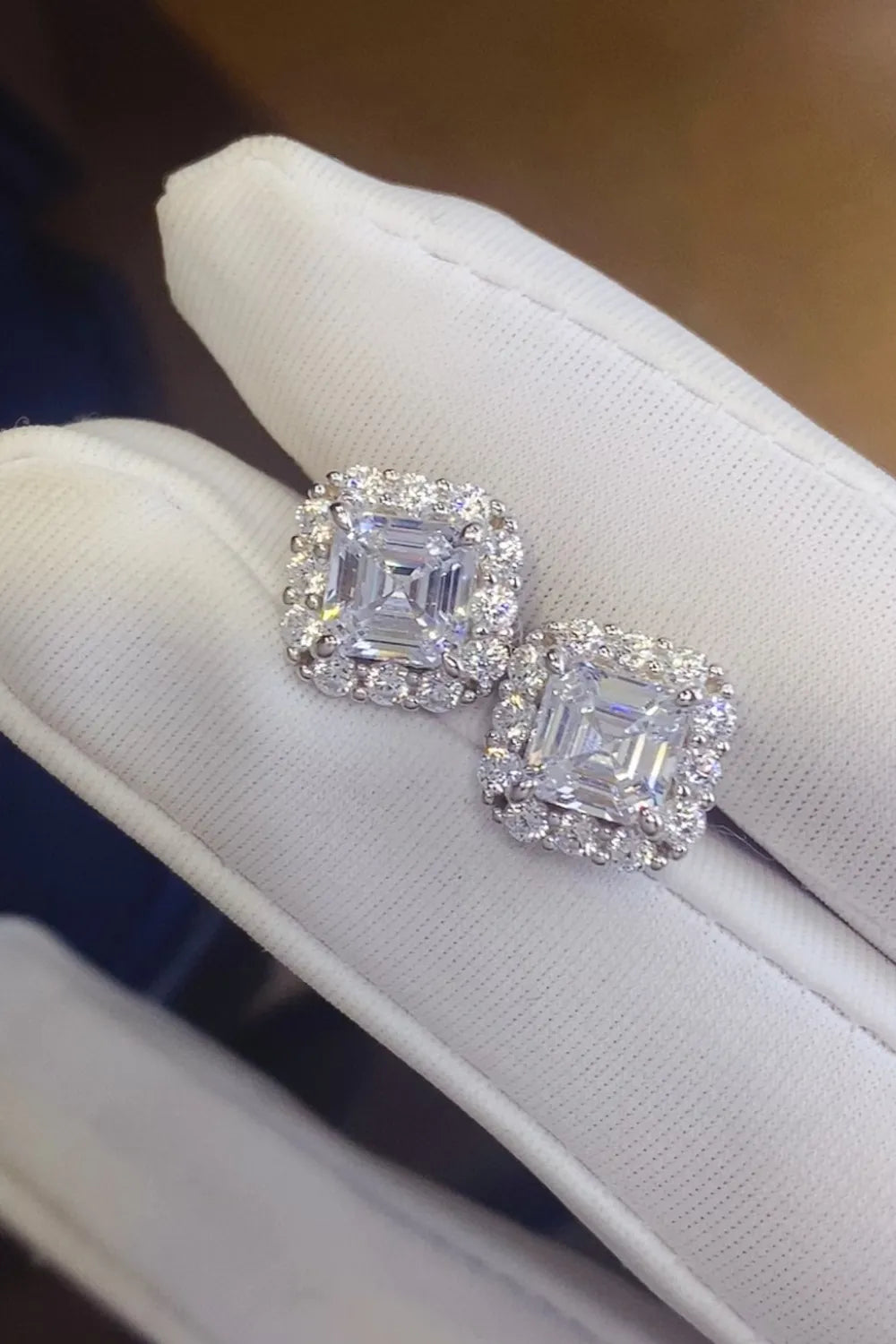 Silver asscher cut halo stud earrings with sparkling cubic zirconia on white fabric.