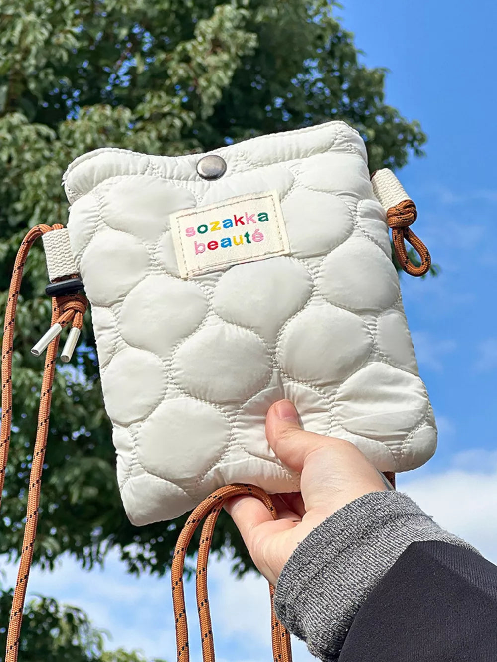 Ivory quilted crossbody bag with adjustable strap and colorful logo patch.