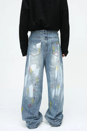 Painterly wash wide-leg denim trousers in medium blue with artistic paint splatters and brushstrokes.