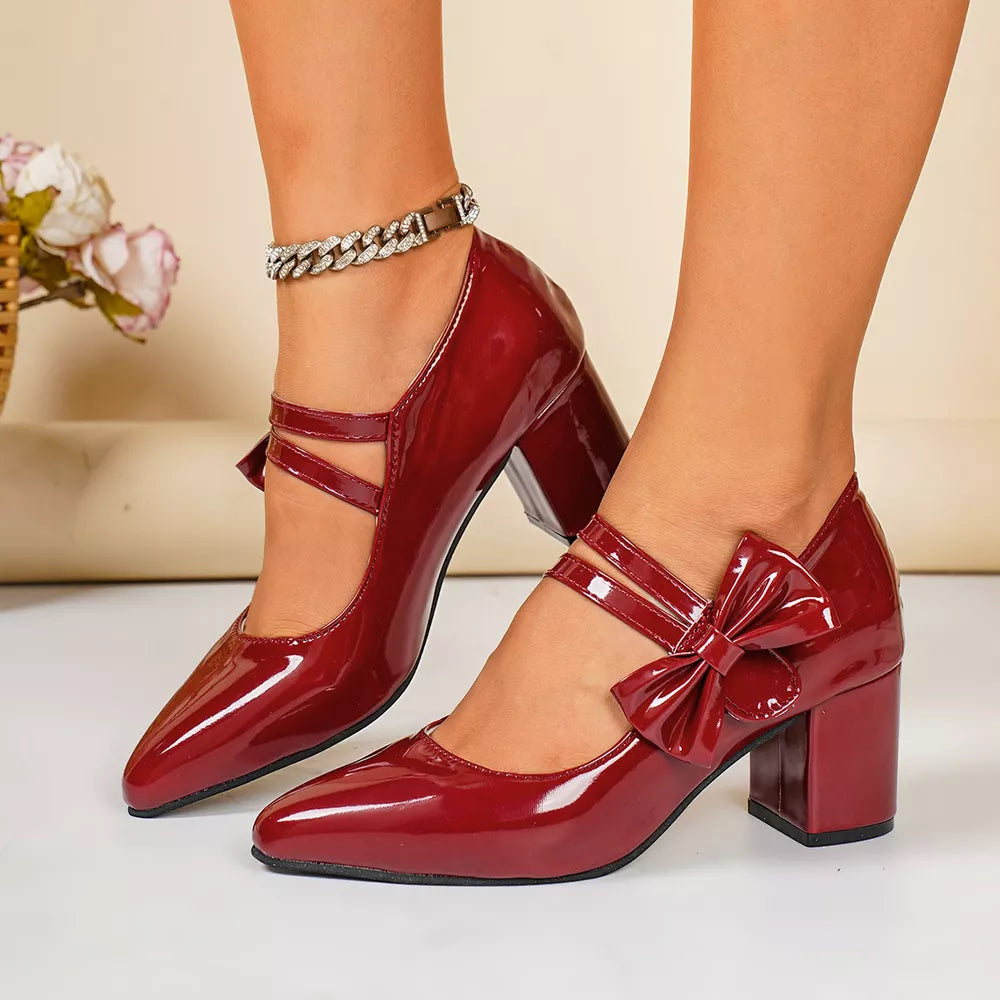 Red patent leather block heel pumps with pointed toe and bow detail.