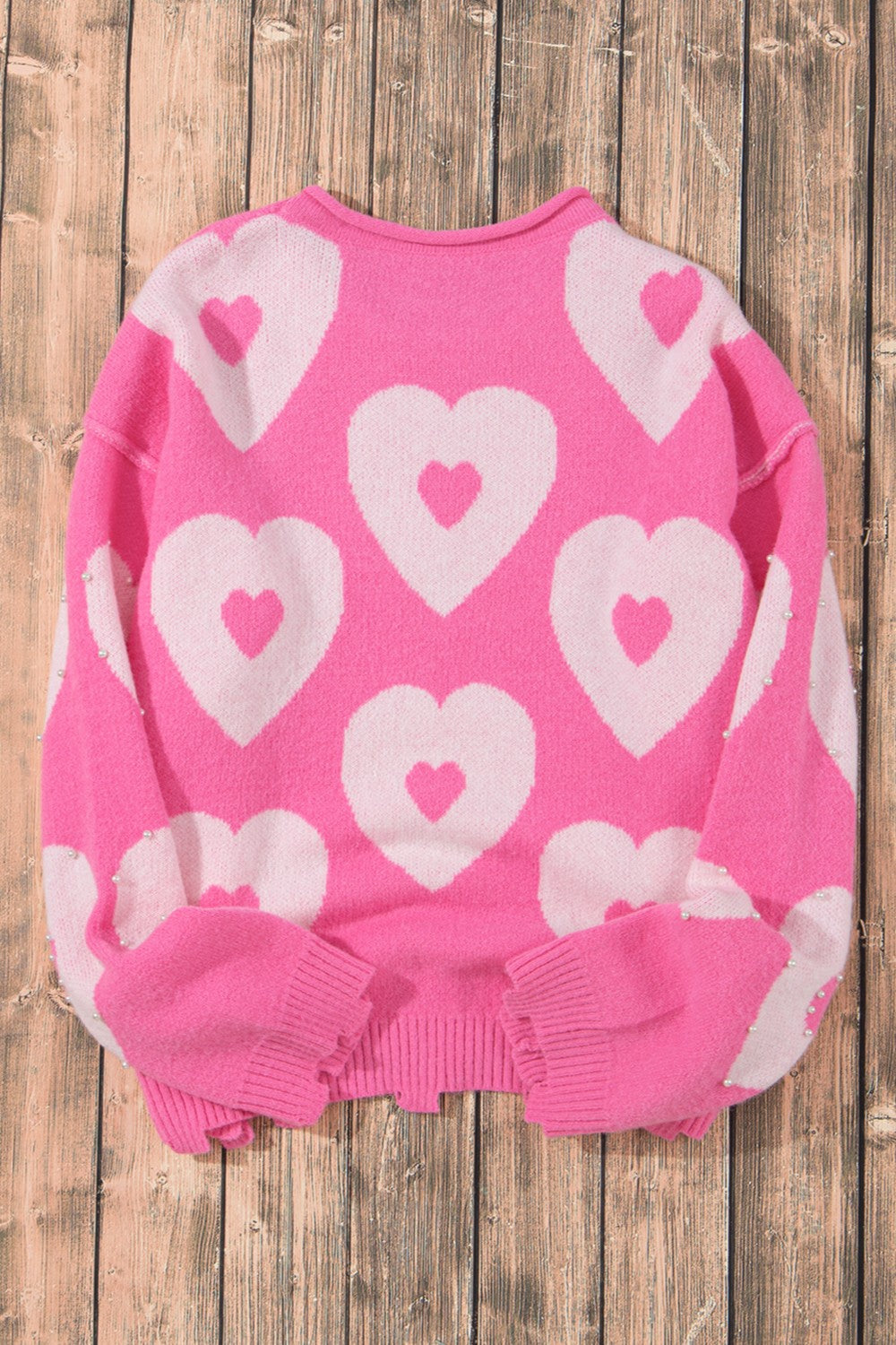 Fuchsia pink knit sweater with allover white heart motif and pearl embellishments on sleeves.