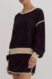 Black sweatshirt and skort set with contrast trim and crew neck, styled with a gold necklace.