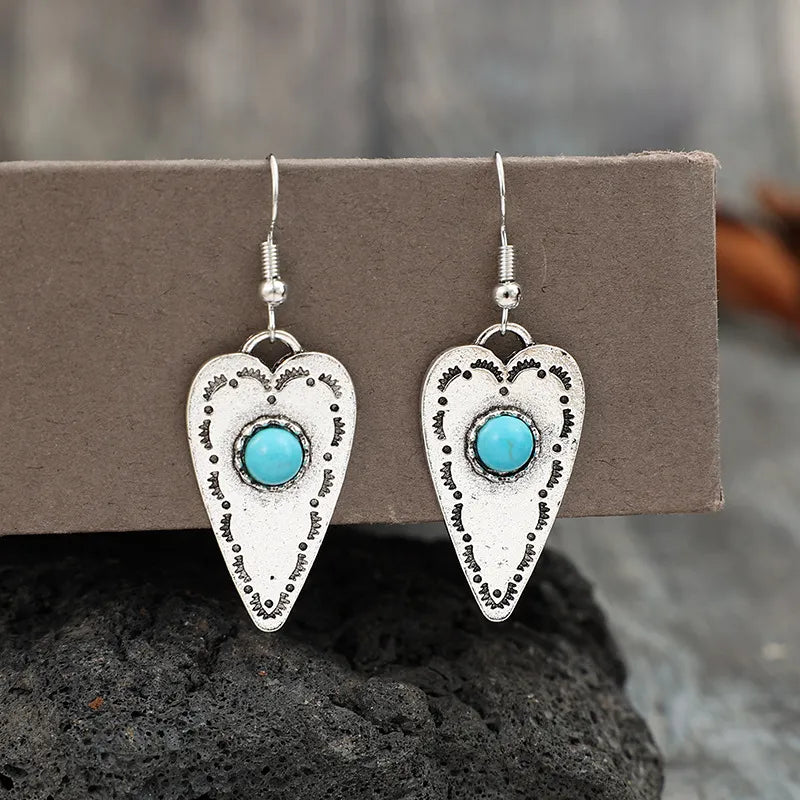 Silver heart-shaped dangle earrings with turquoise stones and tribal etched details.