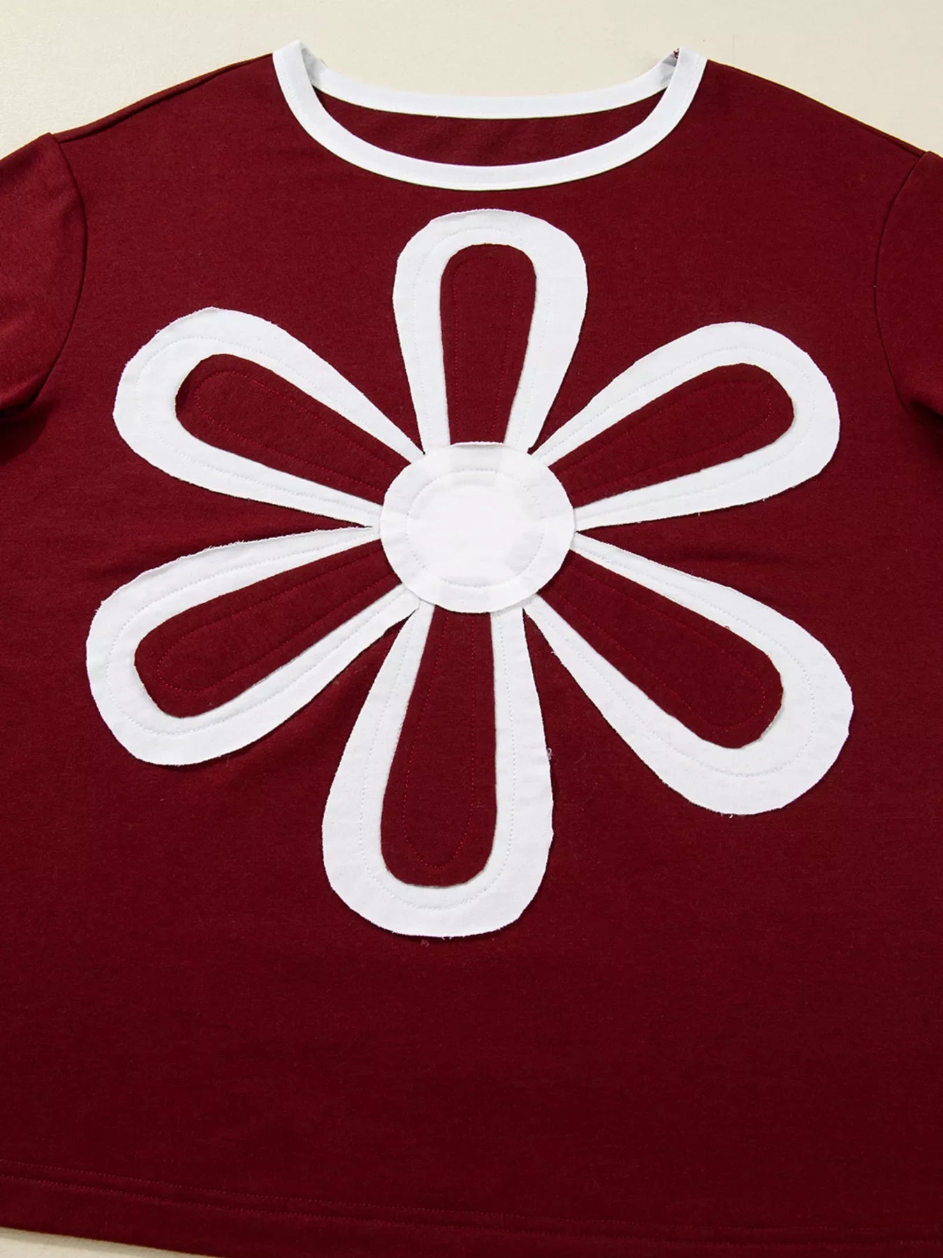 Burgundy long-sleeve top with white flower patch detail and white trim neckline.