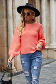 Ribbed knit sweater in coral with balloon sleeves and crew neck, styled with ripped jeans.