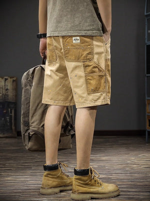 Men's tan cargo shorts with patchwork pockets and paint splatters.