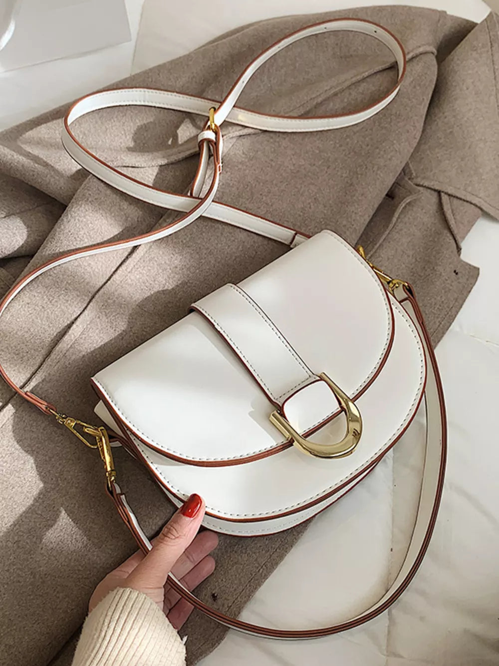 Chic white semi-circular flap crossbody bag with gold buckle detail and brown trim.