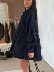 Dark blue denim mini dress with pockets, tiered skirt, and smocked cuffs.