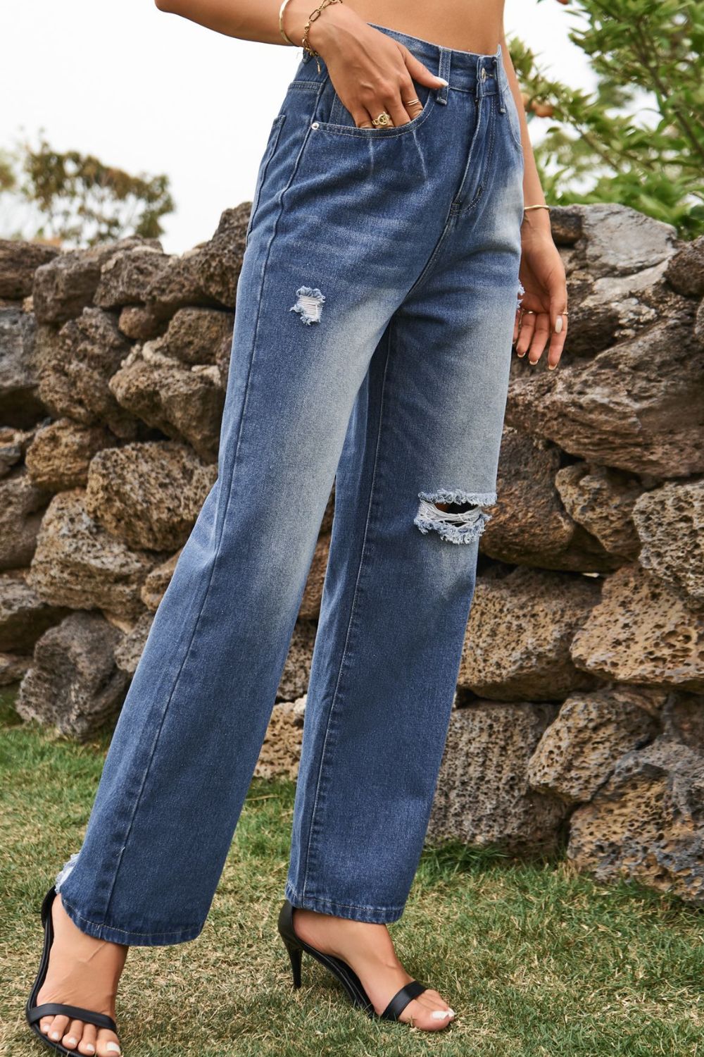 Distressed wide-leg denim trousers in medium wash with ripped details and frayed hem.